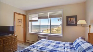 Un dormitorio con cama, cómoda, televisor y ventana con vista a la playa.
