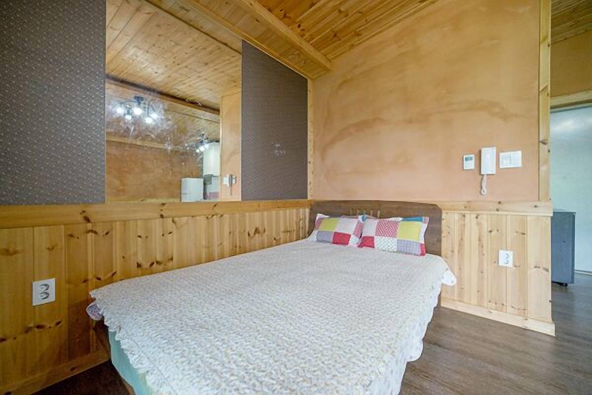 A wooden-paneled room with a bed, a mirror, and a wall-mounted phone.