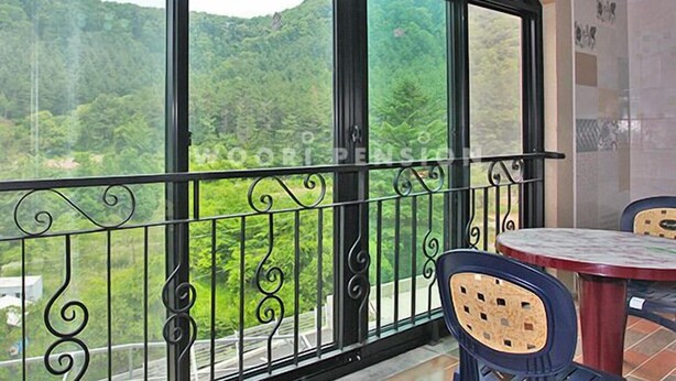 A balcony with a metal railing and two chairs, overlooking a forested hillside. - Yongin Sun & Moon Peension (Yongin)
