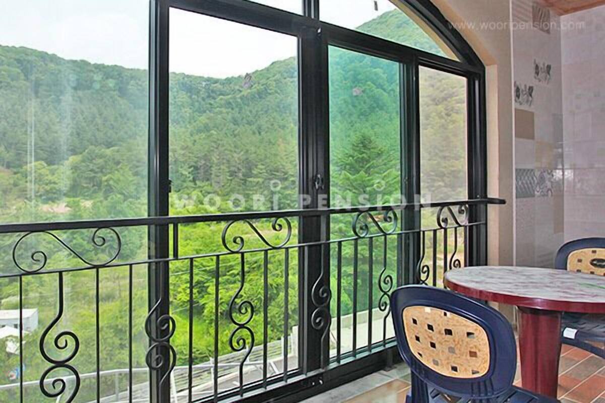 A balcony with a metal railing and two chairs, overlooking a forested hillside.