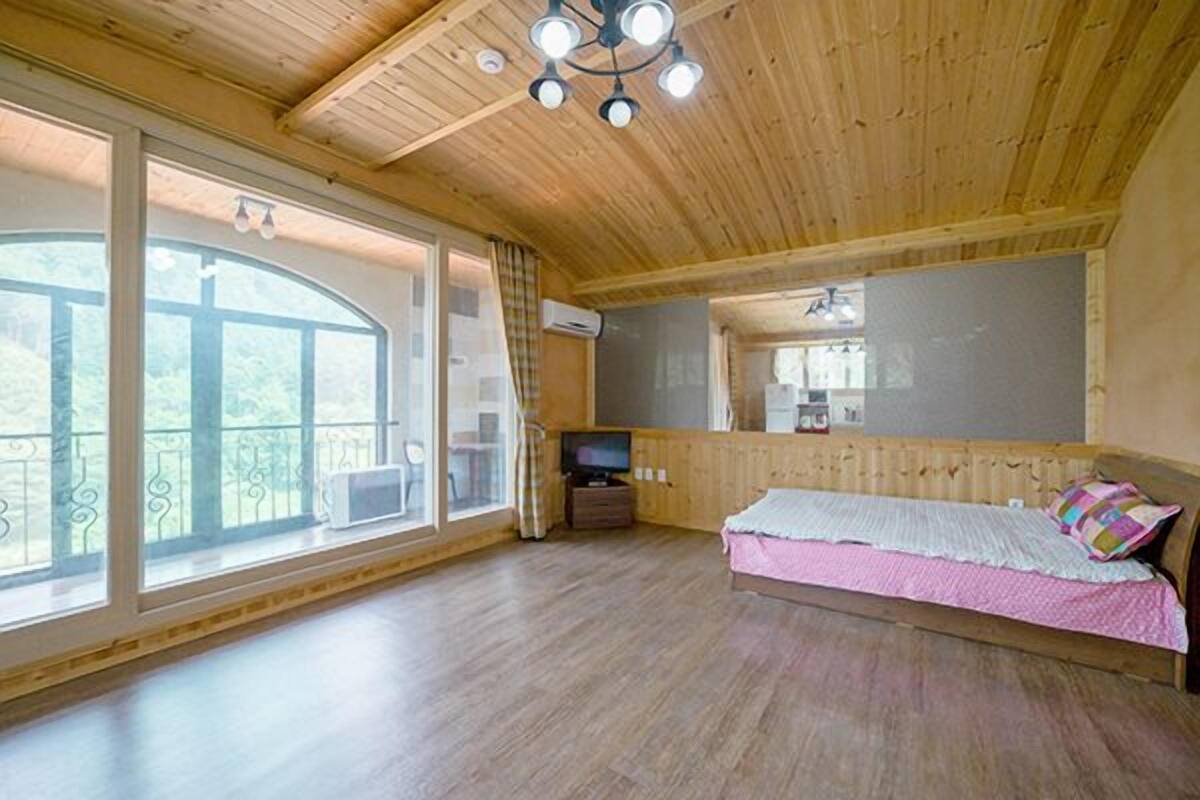 A wooden cabin room with a bed, a TV, and a balcony with a view.