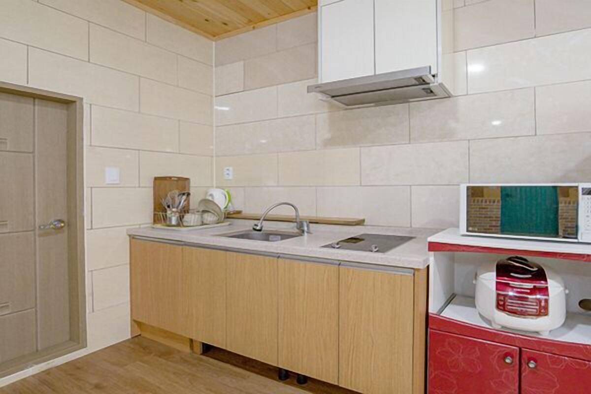 A modern kitchen with a double sink, wooden cabinets, and a microwave on a red countertop.