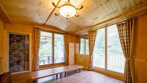A wooden cabin interior with a bench, large windows, and a stone wall. - Yongin Sun & Moon Peension (Yongin)