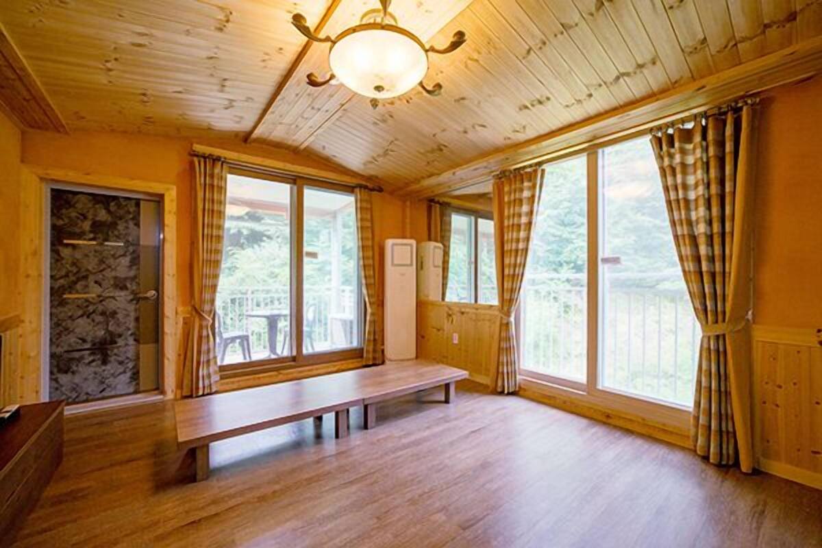 A wooden cabin interior with a bench, large windows, and a stone wall.