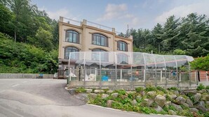 A two-story building with a large glass enclosure, surrounded by greenery and rocks. - Yongin Sun & Moon Peension (Yongin)