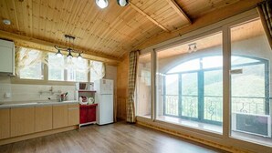 A spacious kitchen with wooden cabinets, a red refrigerator, and large windows offering a view of the outdoors. - Yongin Sun & Moon Peension (Yongin)