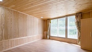 A room with wooden walls and ceiling, large windows with curtains, and a wooden floor. - Yongin Sun & Moon Peension (Yongin)