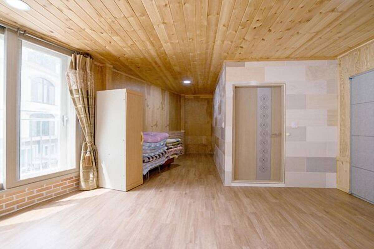 A narrow hallway with wooden flooring, a window with curtains, and a bed with folded blankets.