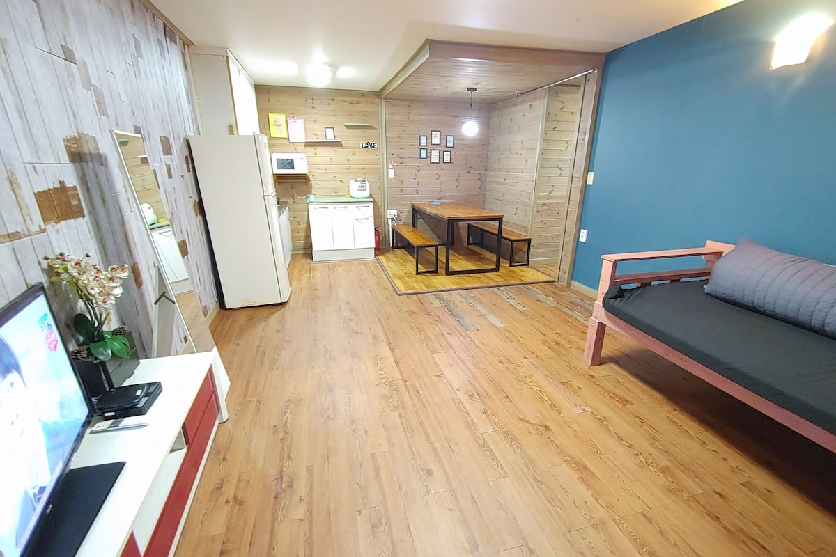 A compact living space with a wooden floor, a sofa, a dining table, and a kitchenette area.