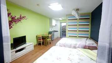 Quarto com duas camas, televisão, uma mesinha e cozinha compacta.