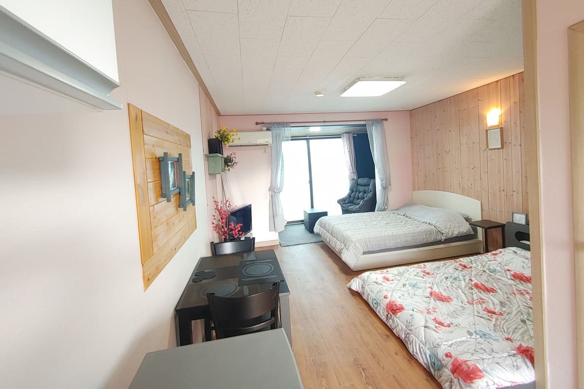 A bedroom with two beds, a desk, a chair, and a window with curtains.