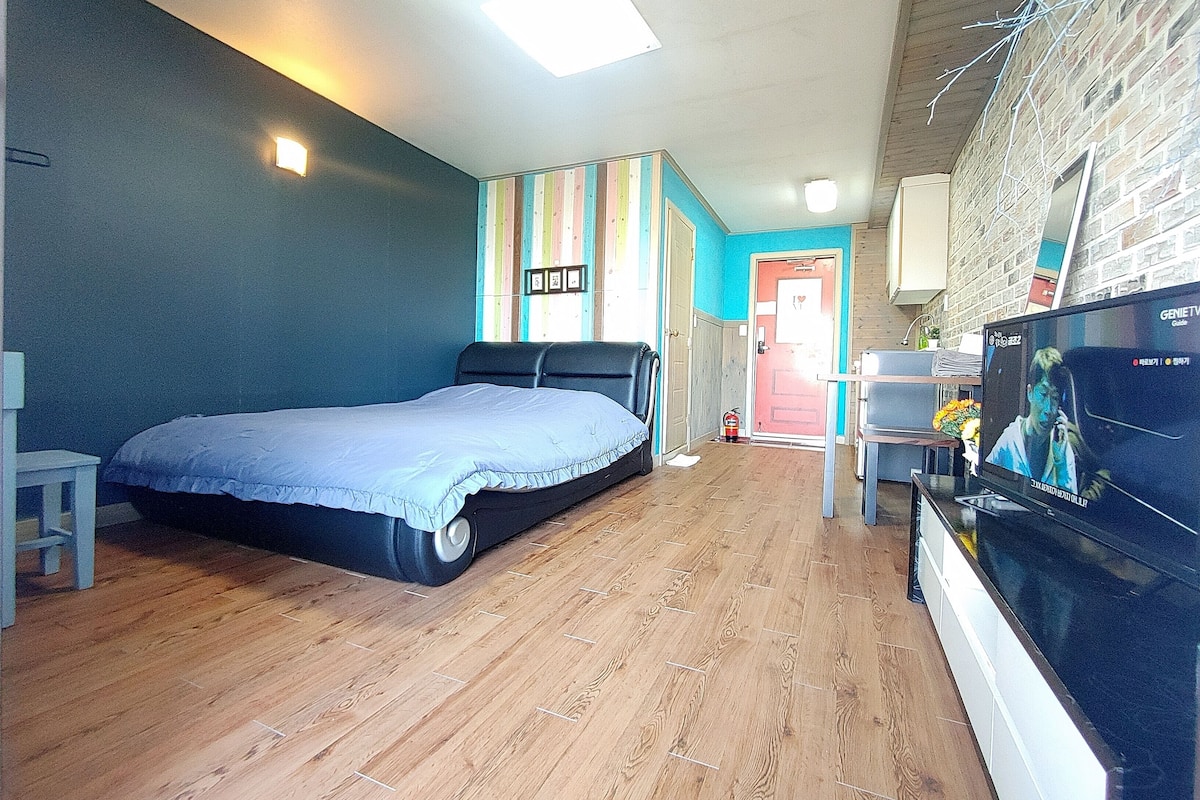 A bedroom with a bed, a TV, and a wooden floor.