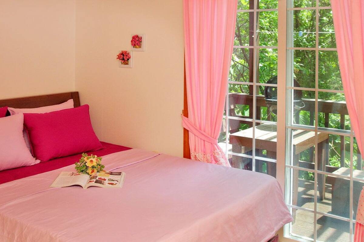Un dormitorio con cama, cortinas rosadas y ventana con vista a un jardín.