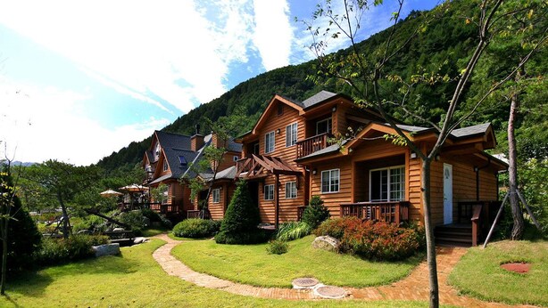 A wooden lodge with multiple rooms, a well-maintained garden, and a mountain backdrop. - Sanwoolrim Pension (Yangyang)