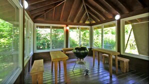 A covered outdoor area with wooden benches, a grill, and large windows offering views of greenery. - Sanwoolrim Pension (Yangyang)