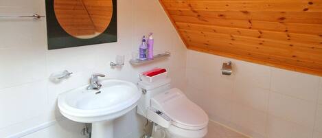 A bathroom with a white sink, toilet, and a wooden ceiling. There are shelves with toiletries and a mirror above the sink.