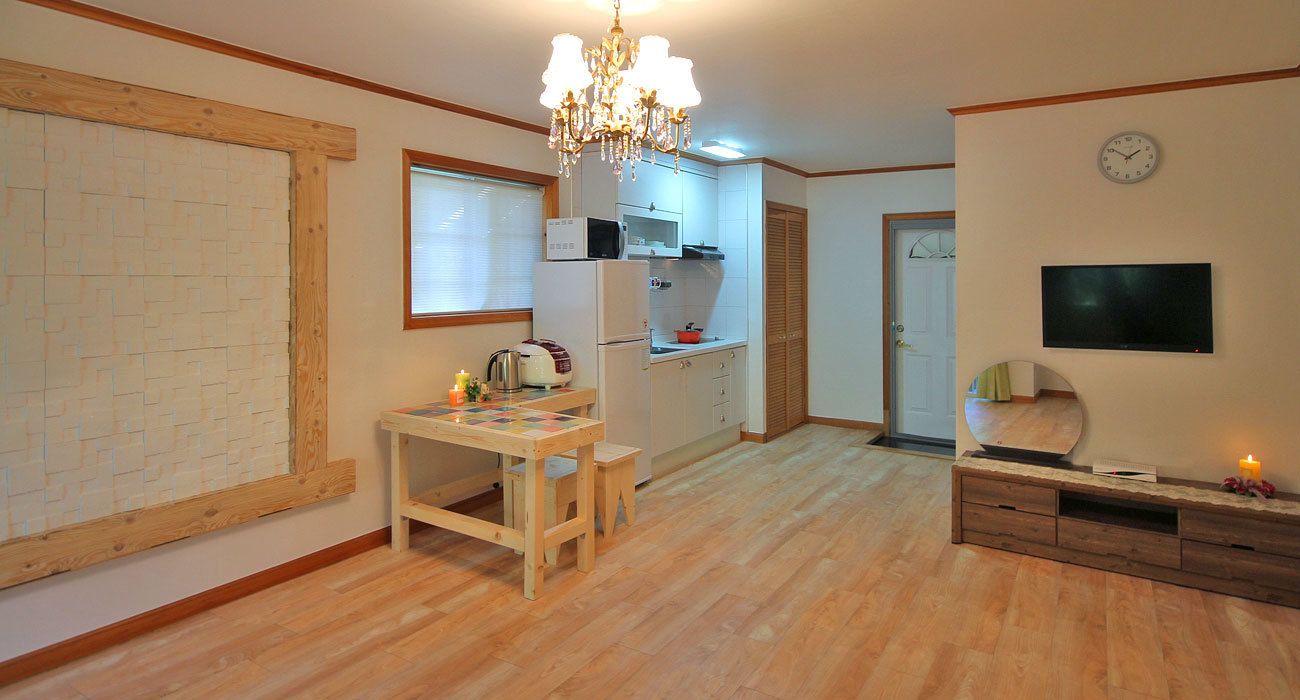 Una cocina con suelo de madera, una araña, un microondas, un refrigerador y un televisor.