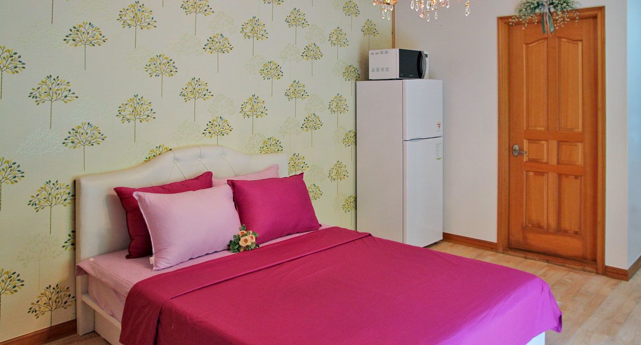 A bedroom with a bed, pillows, a nightstand, a refrigerator, and a wooden door.