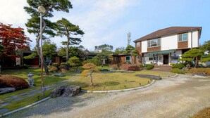 Perinteinen japanilaistyylinen talo, jossa on hyvin hoidettu puutarha, kivipolku, erilaisia pensaita ja pieni lampi.