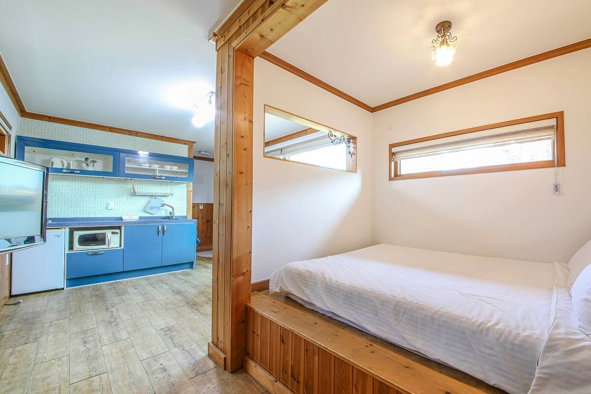 A compact room with a bed, a kitchenette, and a window.