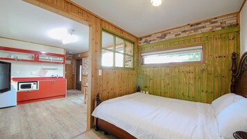Un dormitorio con cabecera de madera, cama con ropa de cama blanca y vistas a una cocina con armarios rojos y microondas.