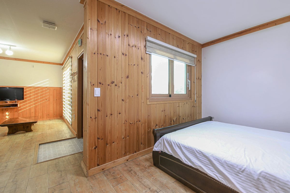 A bedroom with a wooden paneled wall, a single bed, a small table, and a television.