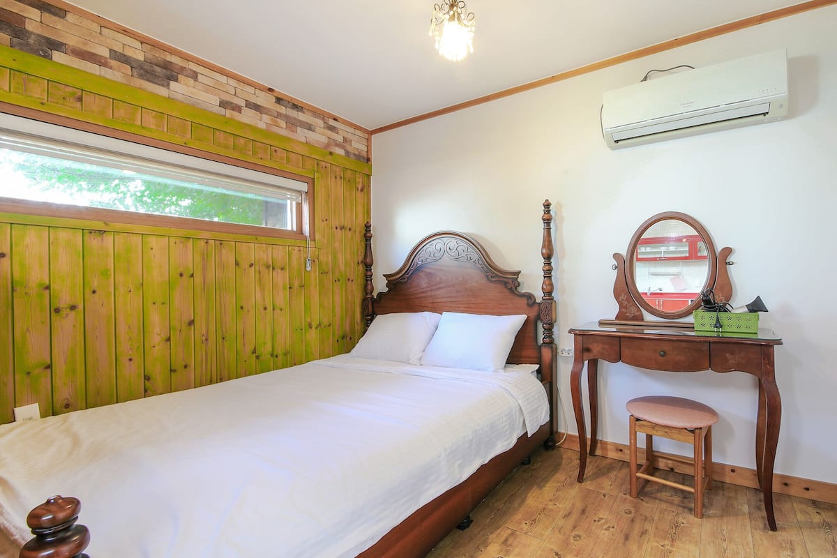 A bedroom with a wooden bed, a wooden dresser with a mirror, and an air conditioning unit on the wall.