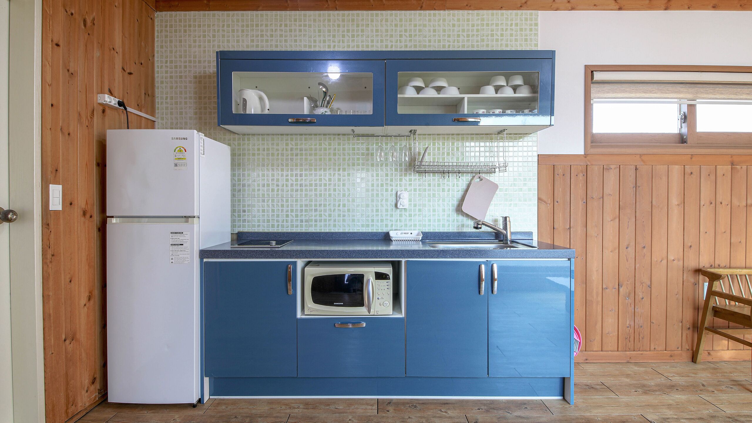 A compact kitchen with a white refrigerator, a microwave, and blue cabinets.