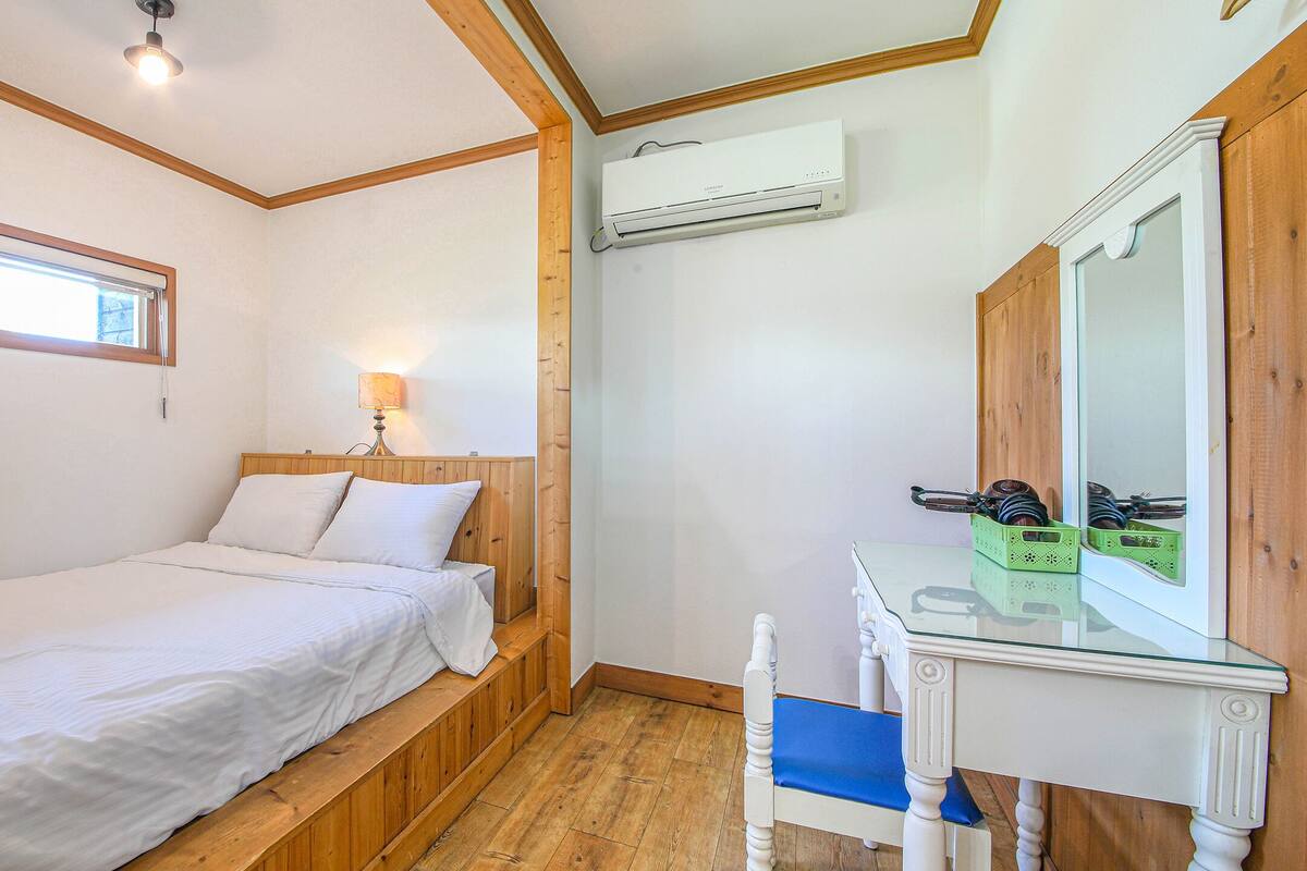A bedroom with a single bed, a nightstand, a mirror, and a window.