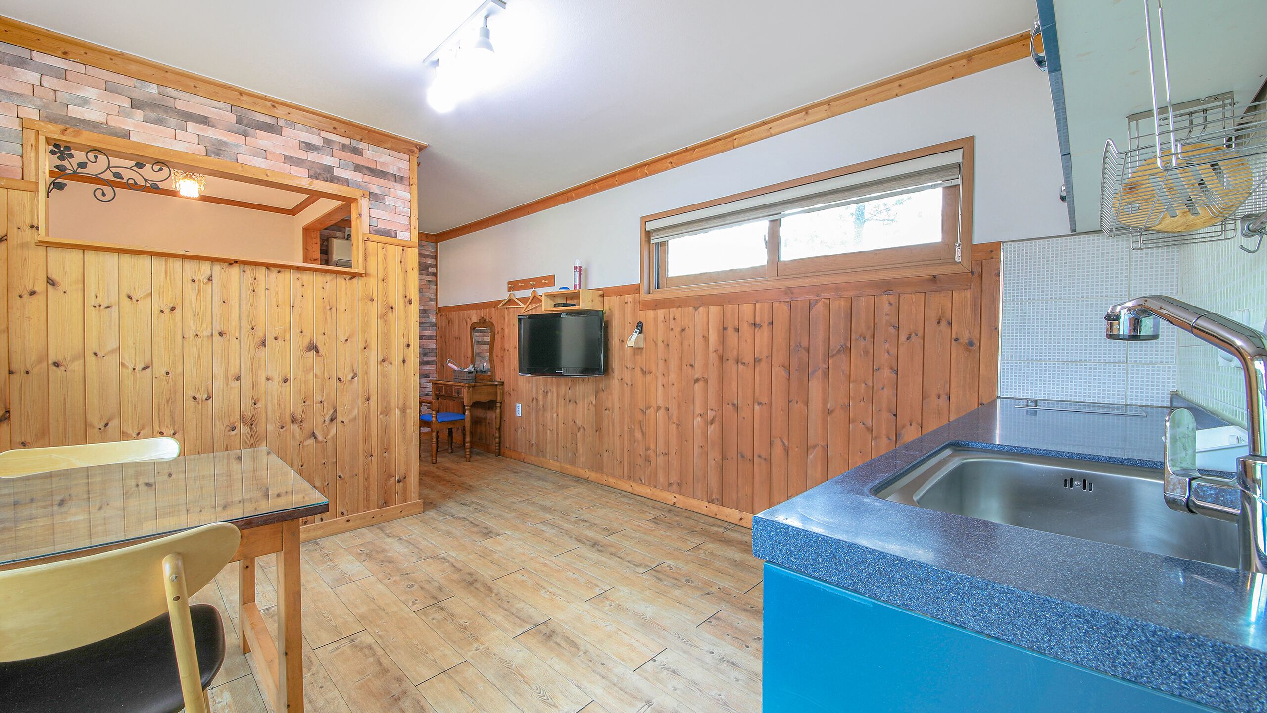 A kitchen with wooden walls, a blue countertop, a sink, and a window.