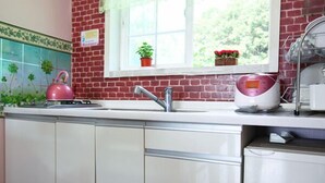 A kitchen with a brick wall, a window with plants, a pink kettle, and a dish rack. - Yongin Doongji Art Village Pension (Yongin)