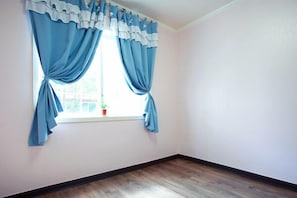 A room with a window, wooden flooring, and a white wall.