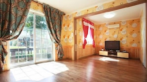 A spacious living room with a large sliding glass door leading to a balcony, a flat-screen TV, and wooden flooring. - Yongin Doongji Art Village Pension (Yongin)