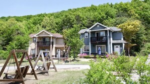 A two-story house with a balcony, surrounded by lush greenery and a clear sky. - Yongin Doongji Art Village Pension (Yongin)