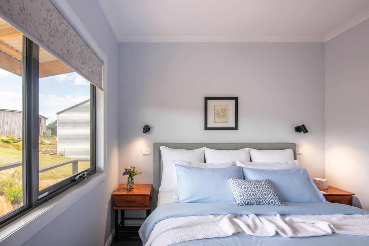 A bedroom with a bed, a nightstand, a window, and a framed picture on the wall.