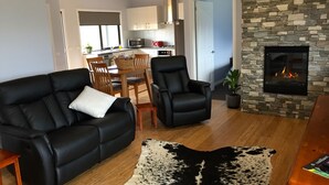 A modern living room with a black leather sofa, a black armchair, and a stone fireplace.