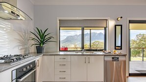 A modern kitchen with white cabinets, a stainless steel dishwasher, and a large window offering a mountain view.