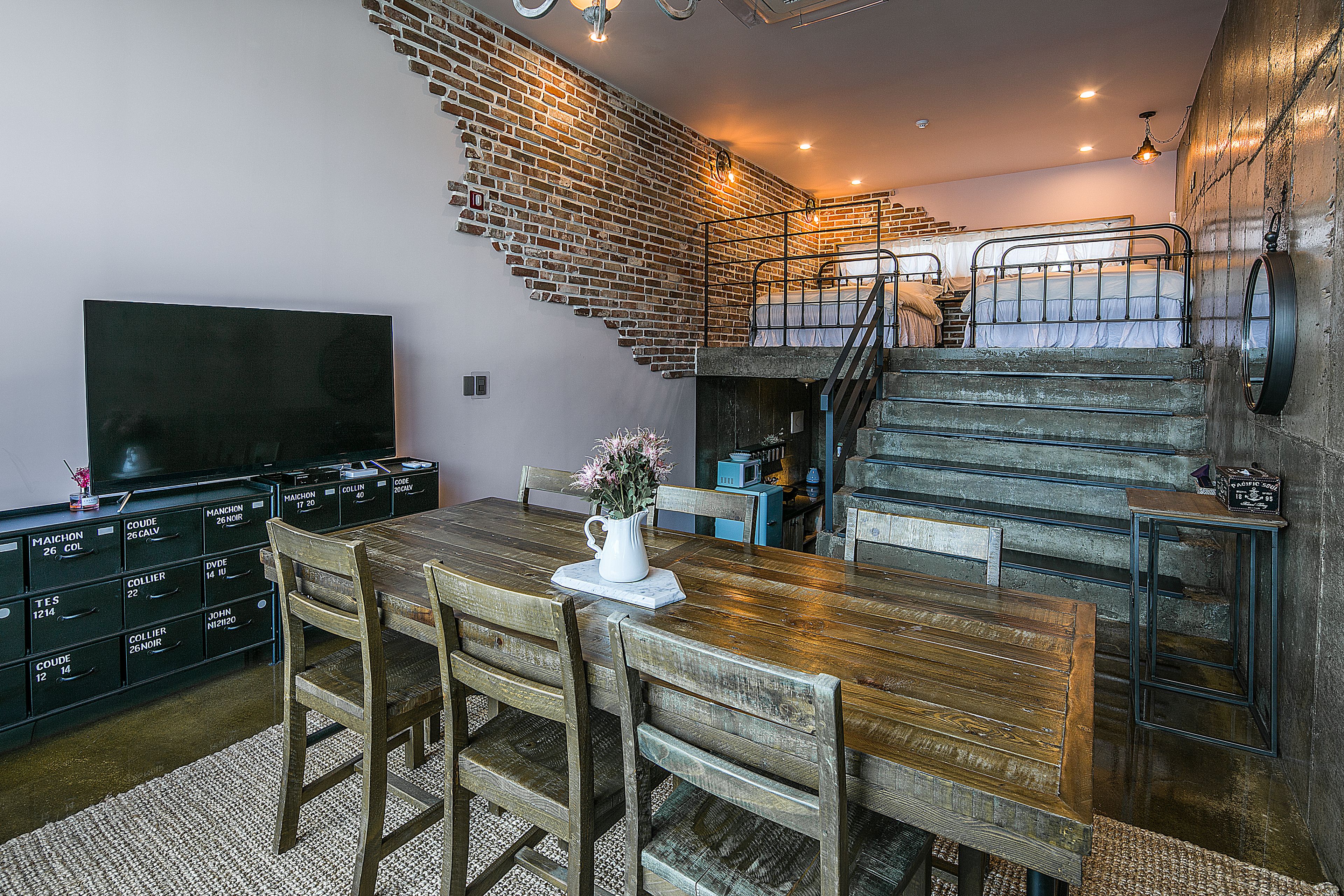 Ein Essbereich mit Holztisch und -stühlen, einem Fernseher an der Wand und einer Treppe, die in eine obere Ebene führt.