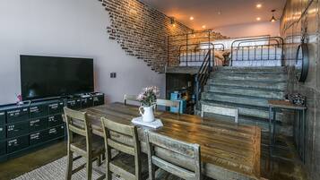 Ein Essbereich mit Holztisch und -stühlen, einem Fernseher an der Wand und einer Treppe, die in eine obere Ebene führt.