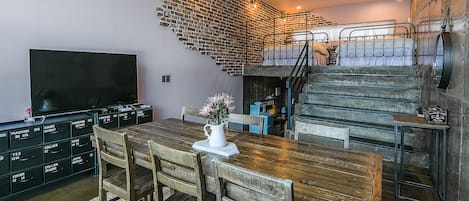 Un comedor con una mesa y sillas de madera, un televisor en la pared y una escalera que sube a un nivel superior.