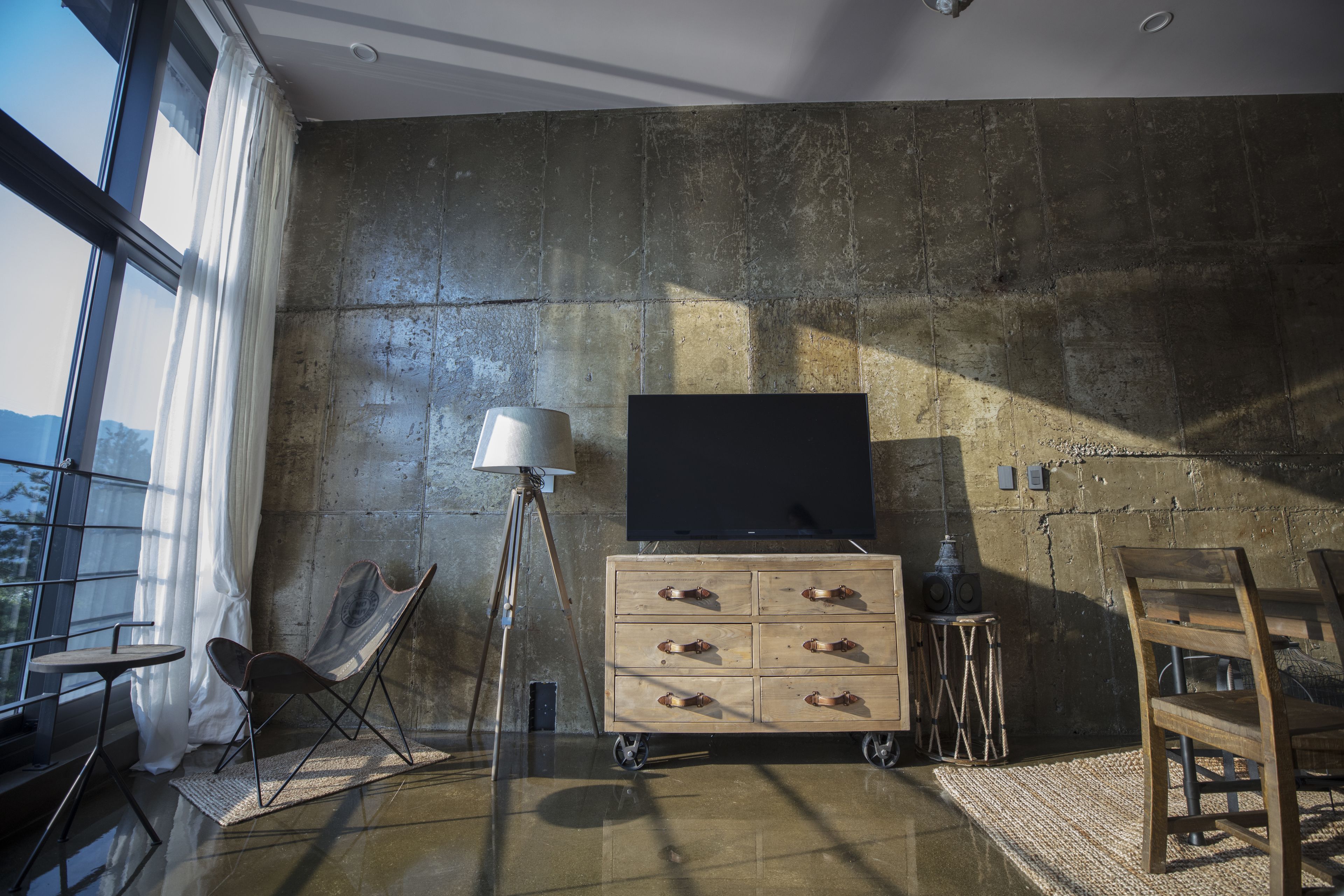 Een moderne kamer met een groot raam, een houten kast, een stoel en een lamp.
