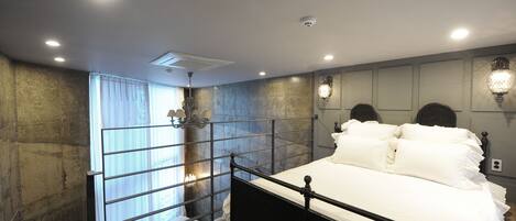 Un dormitorio con estructura de cama metálica, un ventanal con cortinas y apliques de pared.