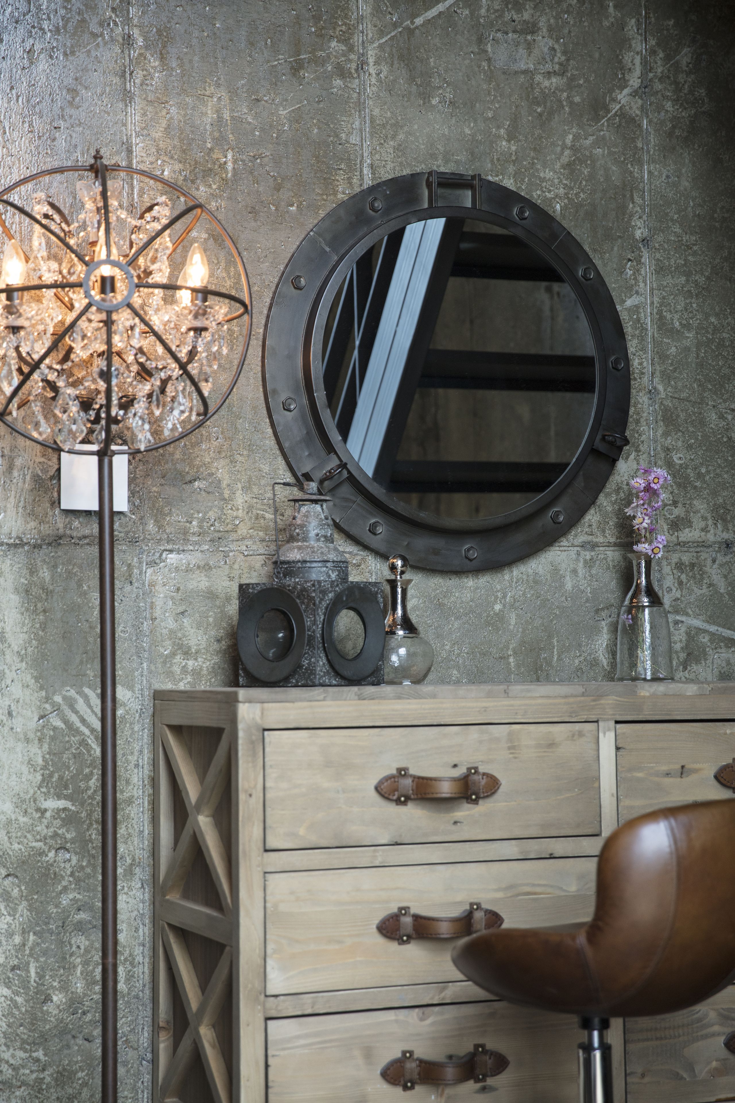 A vintage-style room with a wooden dresser, a leather chair, a round mirror, and a unique chandelier.
