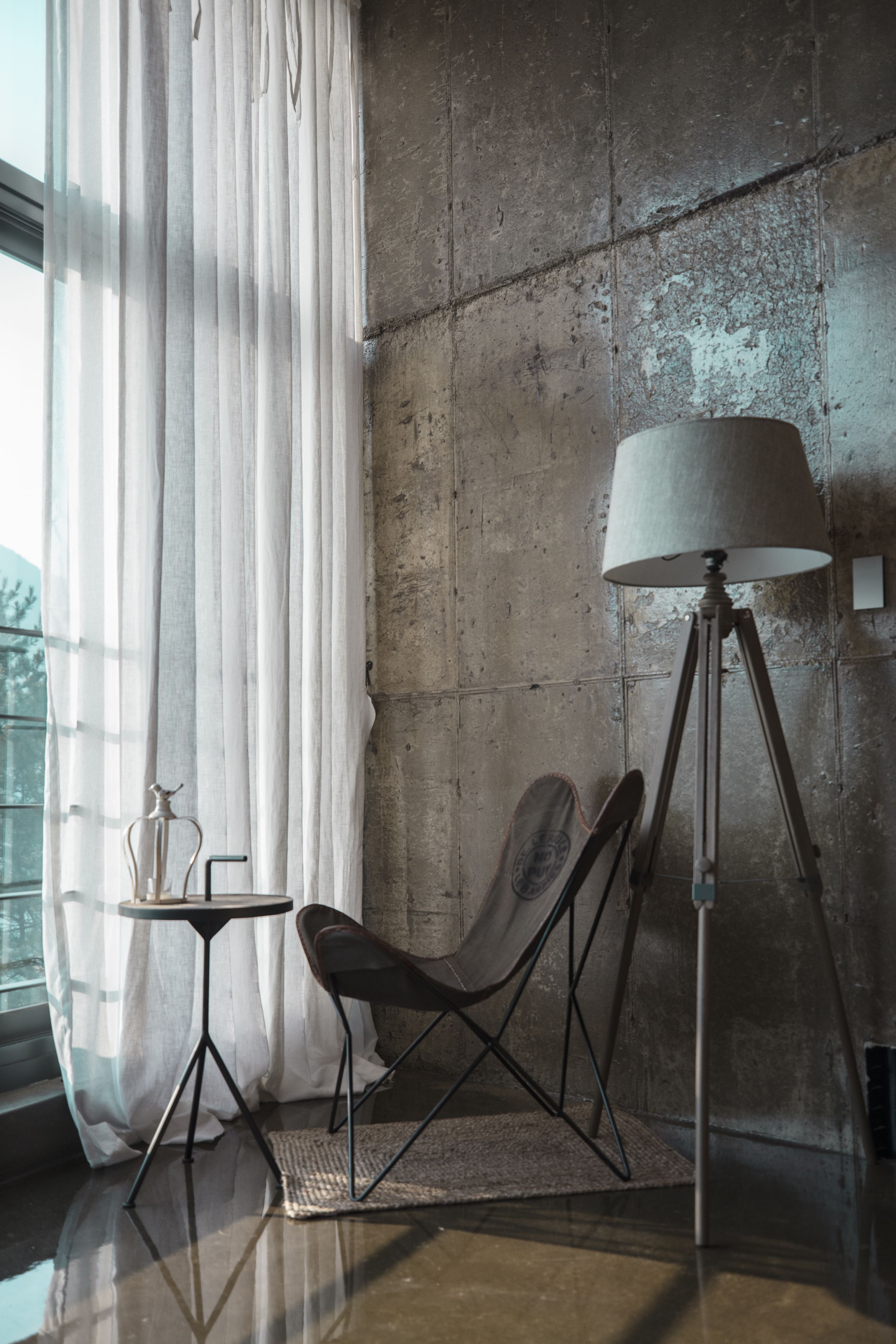 Een moderne kamer met een betonnen muur, een vloerlamp, een klein tafeltje en een stoel.