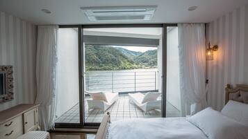 A bedroom with a bed, a nightstand, a dresser, and a view of a balcony with a railing and chairs.
