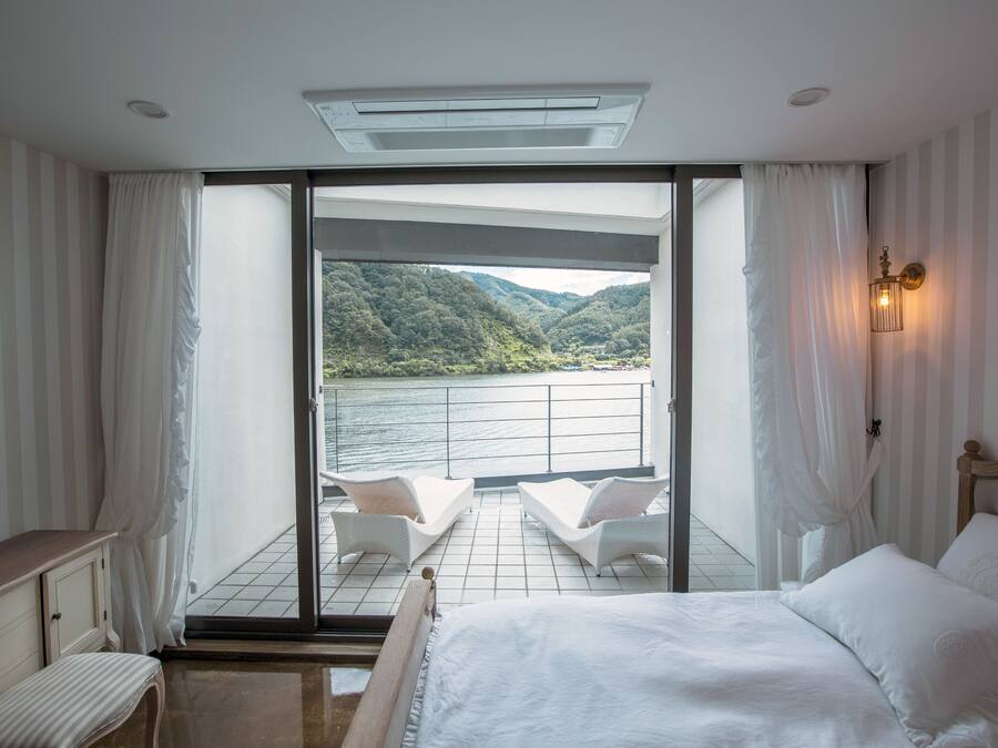 A bedroom with a bed, a nightstand, a dresser, and a view of a balcony with a railing and chairs.