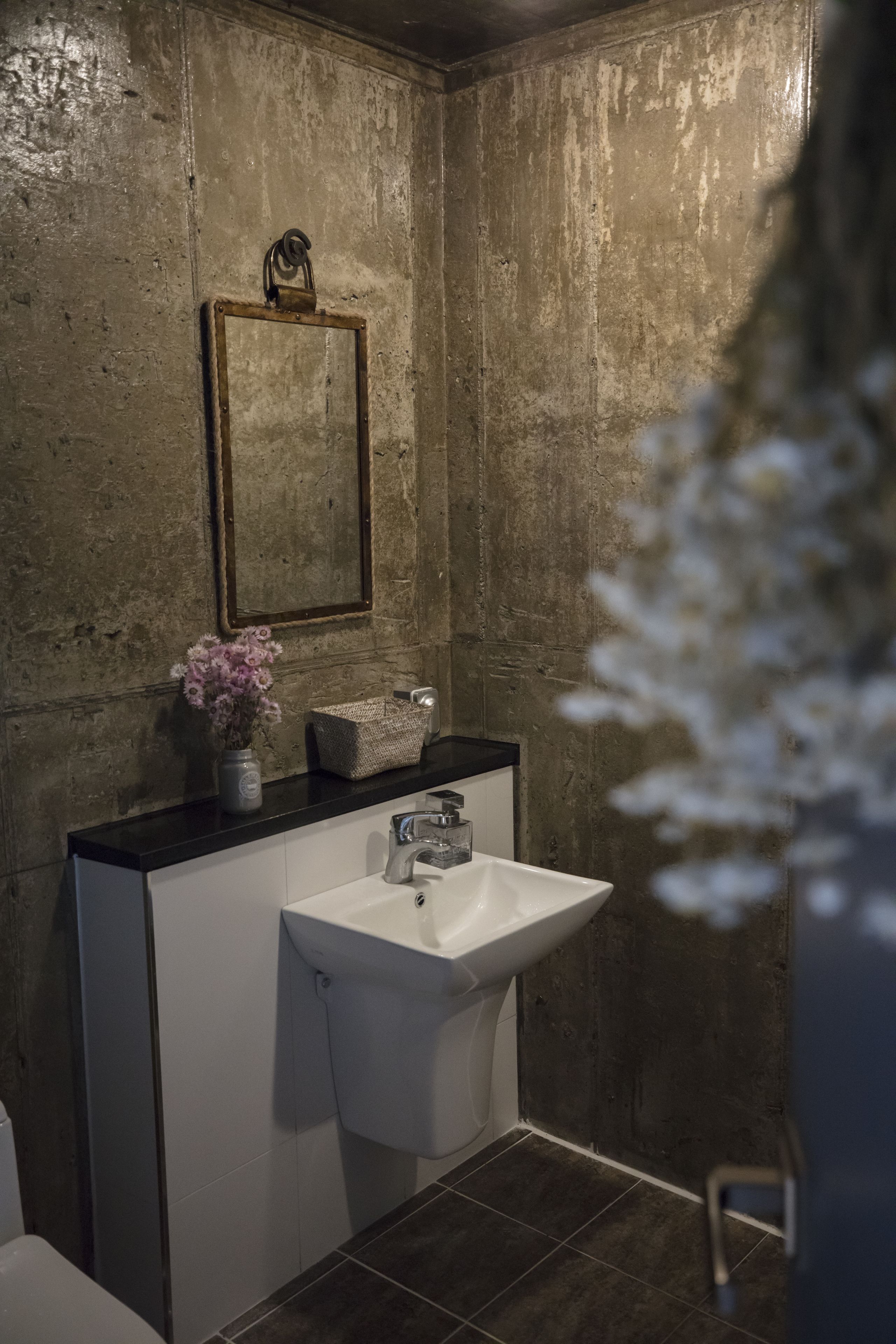A bathroom with a white sink, a mirror, and a vase with flowers on the countertop.