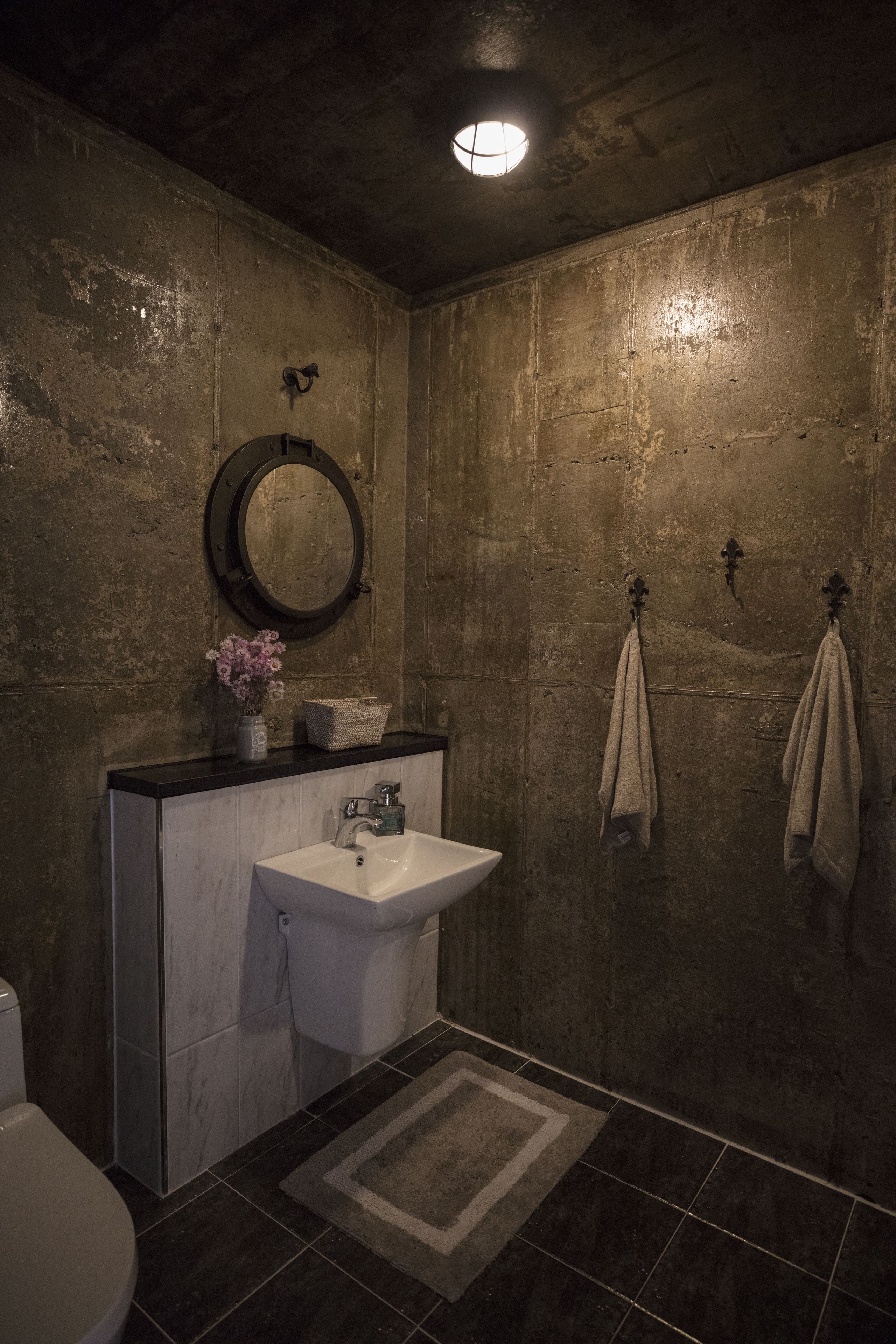 A bathroom with a white sink, a round mirror, and two towels hanging on hooks.