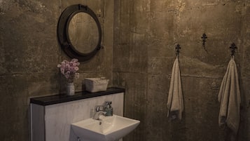 A bathroom with a white sink, a round mirror, and two towels hanging on hooks.