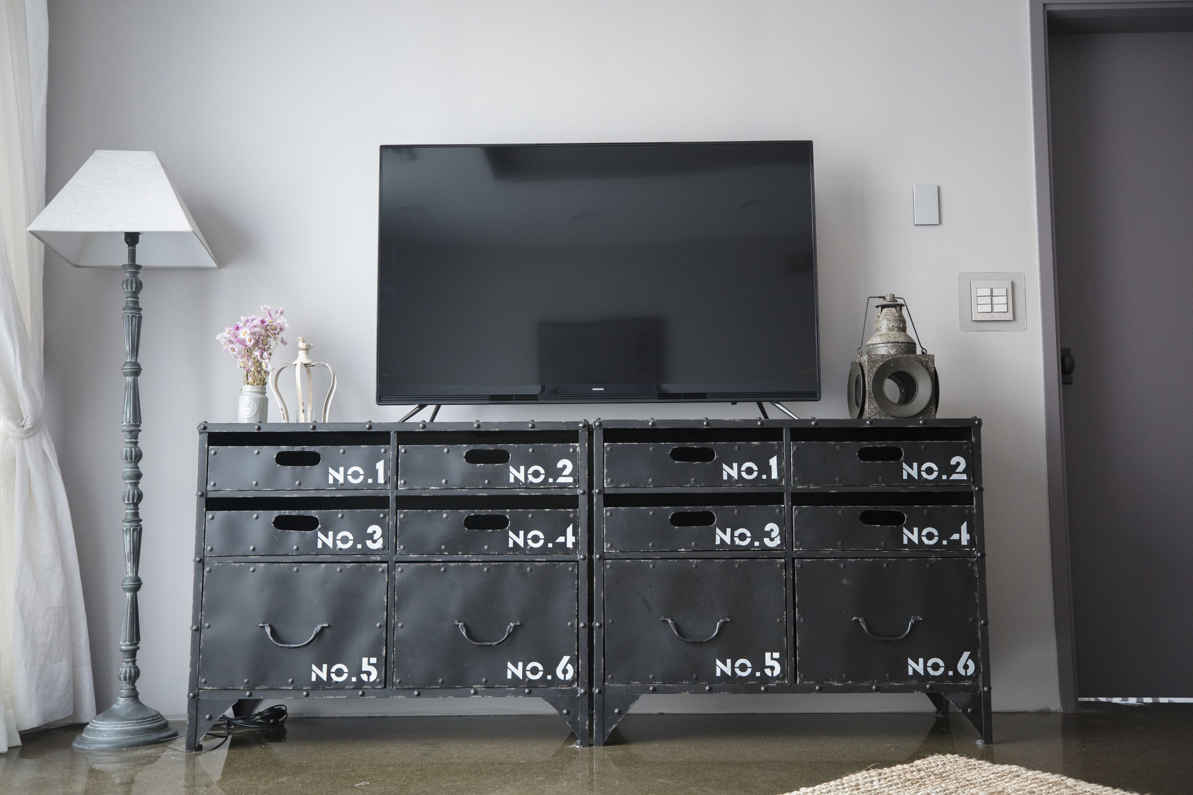 Un mueble de televisión de metal negro con compartimentos numerados y un televisor de pantalla plana.